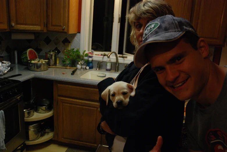 two people hold an adorable dog in a kitchen