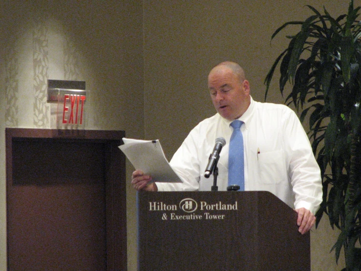 man standing at podium with papers in front of him