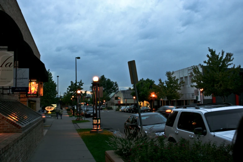 a city street scene at dusk with cars parked in the parking lot