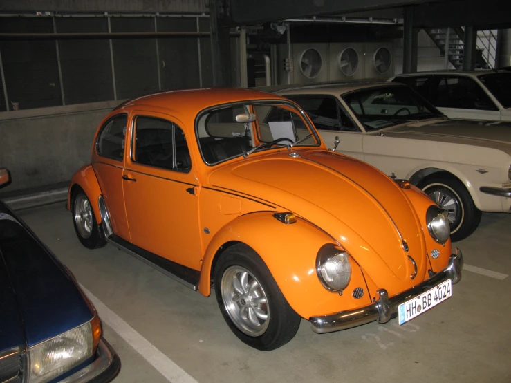 the front of an orange volkswagen beetle with two white cars behind it