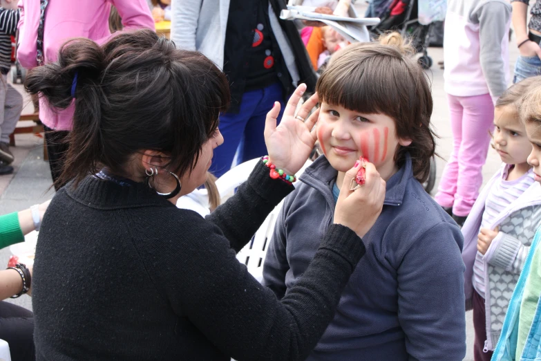 woman putting powder on child's face next to crowd