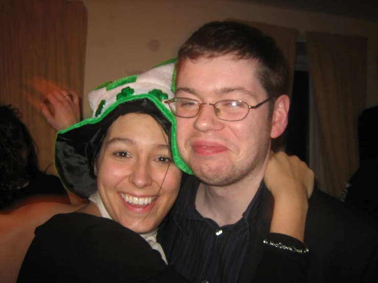 a woman wearing a green hat poses next to a man in glasses