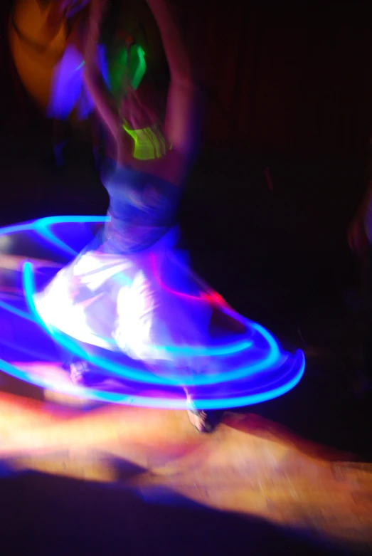 a woman spins a neon hula hoop in the dark