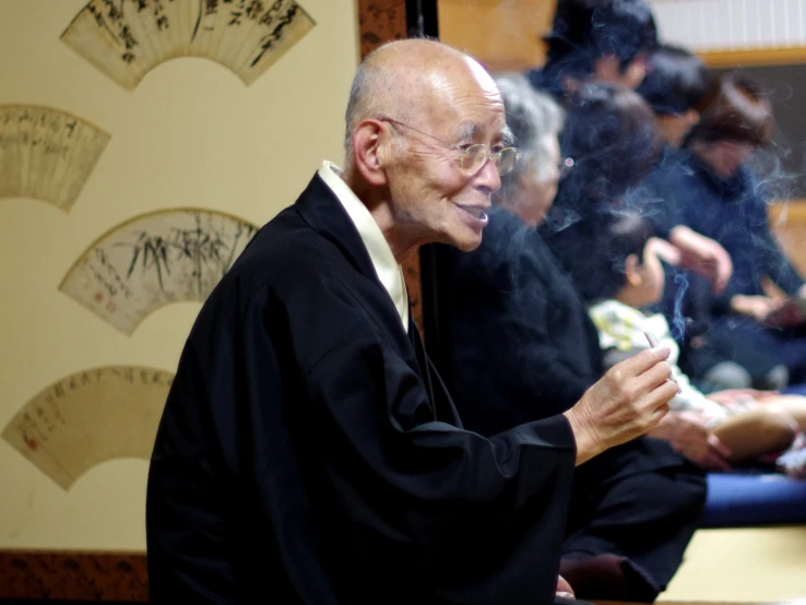 an older man holding a cigarette with others sitting around him