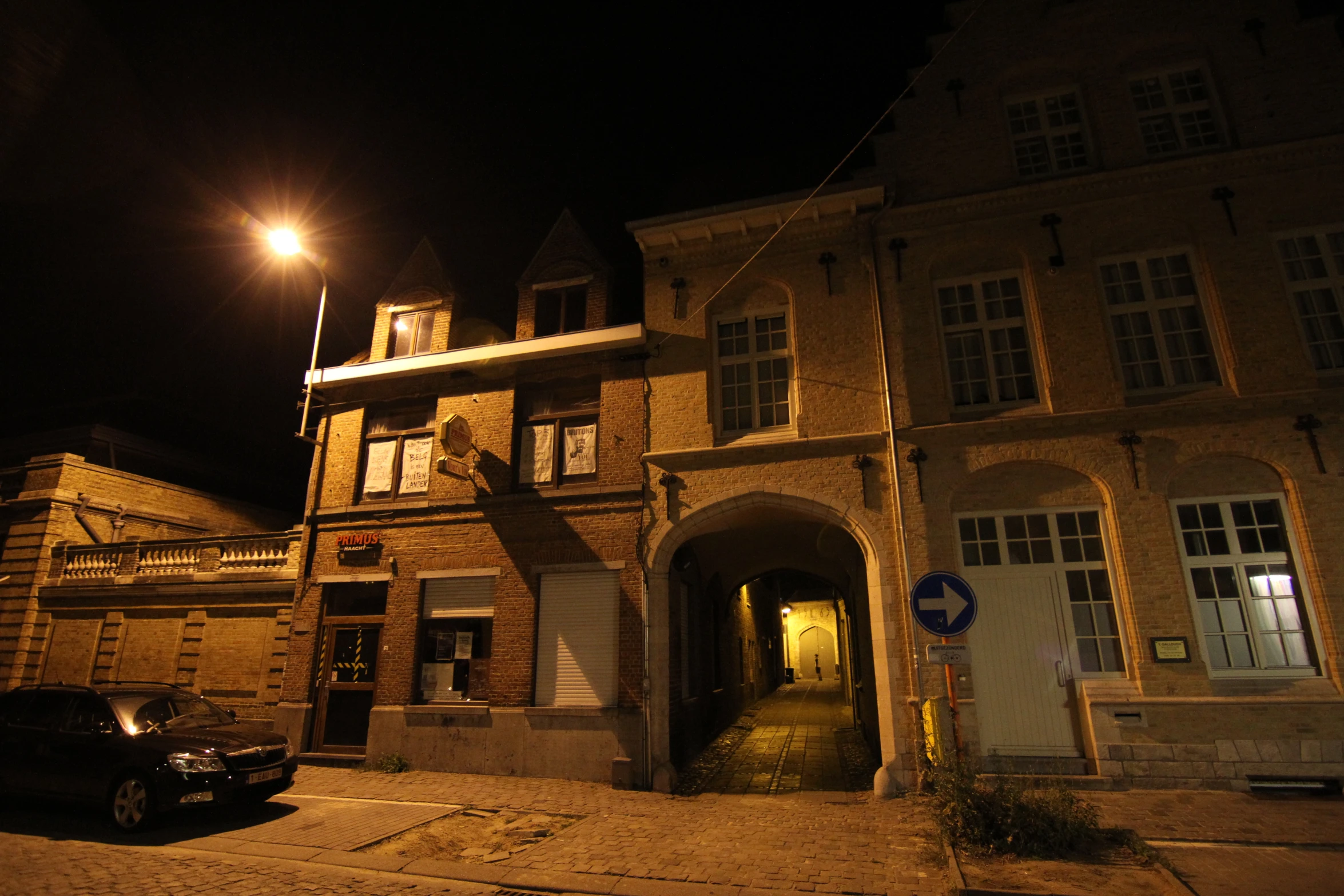 a street side view at night with one car parked on the side and another car out front