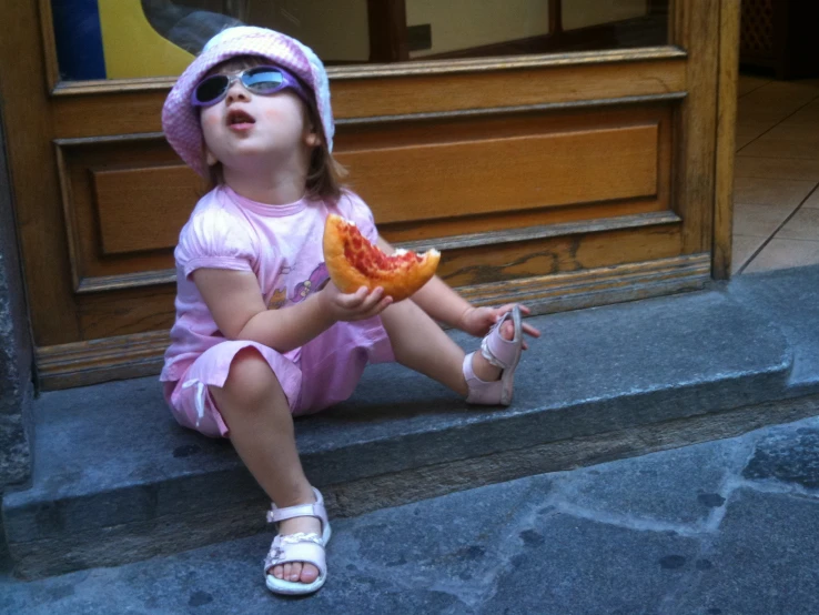 little girl sitting on steps holding a slice of pizza