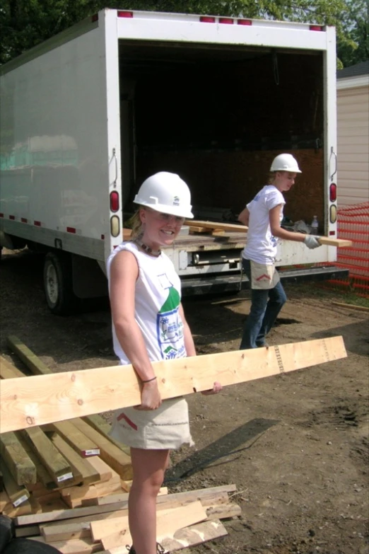 a woman stands next to a trailer holding lumber