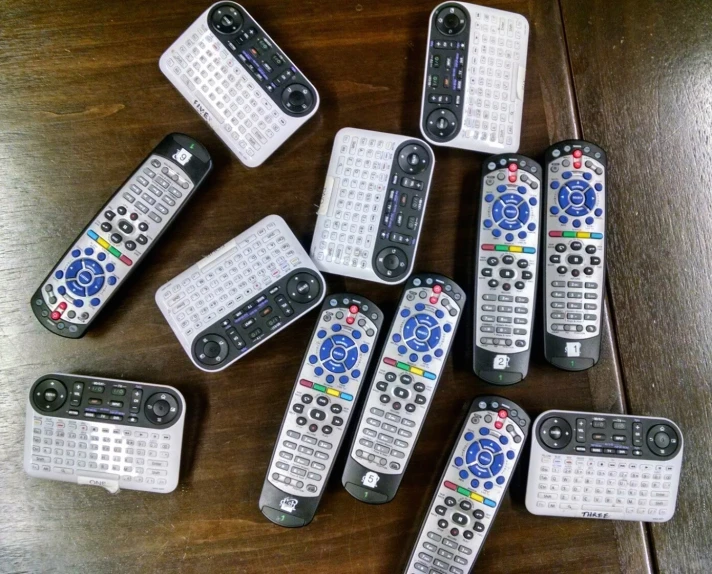 eight remote controls sitting on a wooden table