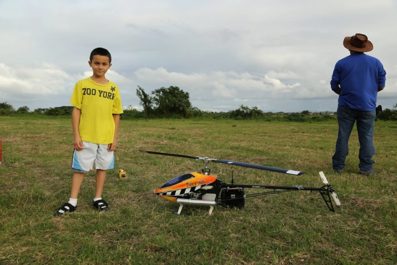 some boys standing around a remote control helicopter in the grass