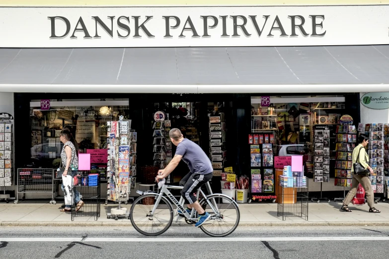 a man riding his bicycle down the street past a store