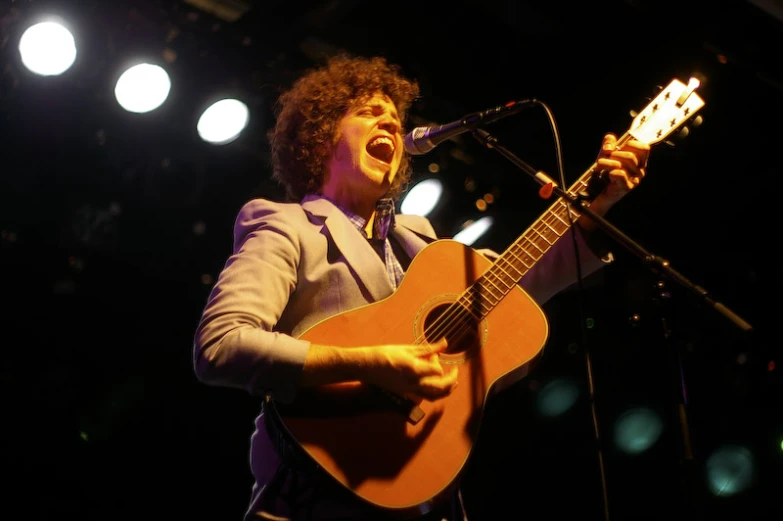 a man in a suit and tie singing while holding a guitar