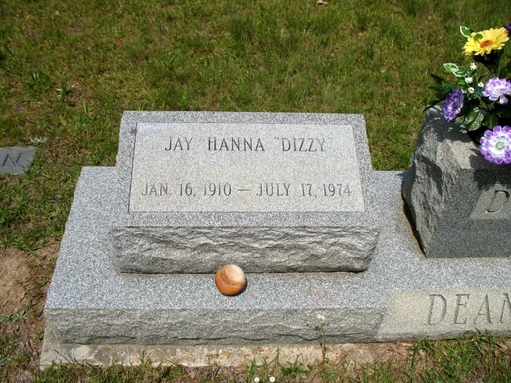 a headstone sits in the grass beside a small ball and flowers