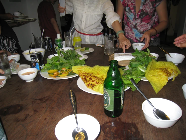 a table with plates and silverware with plates and silverware with vegetables on them and people pouring water into bottles