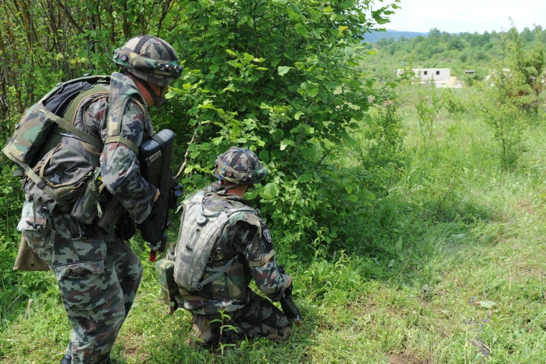 two soldiers on the edge of a field picking leaves