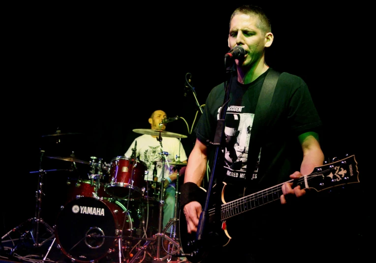 a man singing on a stage with a guitar and drums