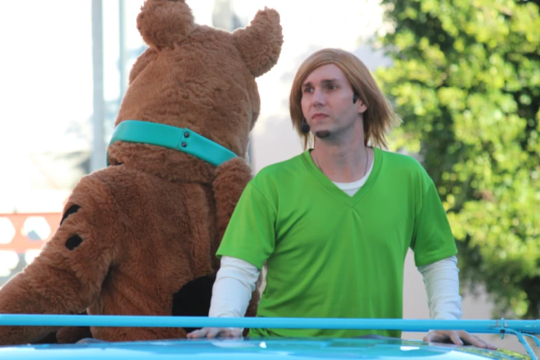 man walking past a large stuffed animal in green shirt