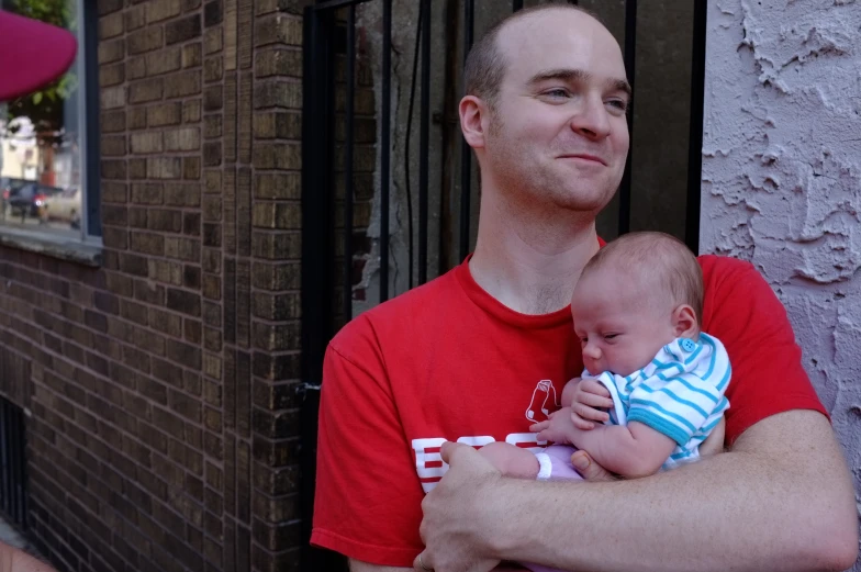 a man standing next to a brick wall with a baby in his arms