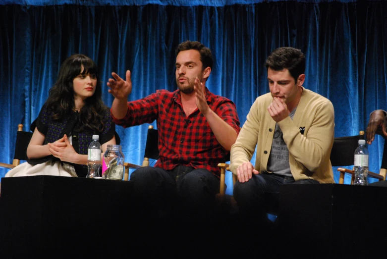 three people sitting on chairs and a man with his hands up