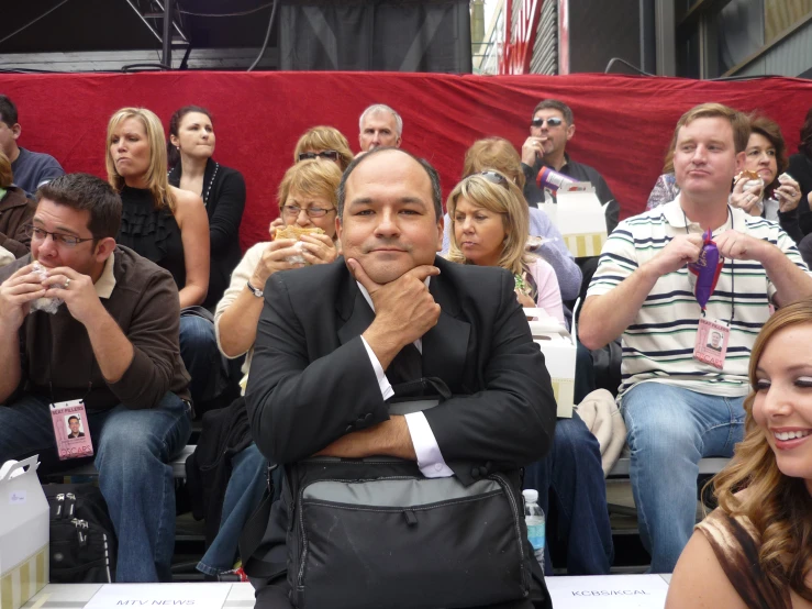 a man with glasses and a suit sits in front of a crowd