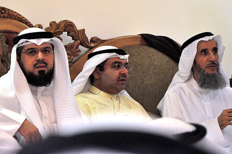 three men sitting down on a wooden bench talking