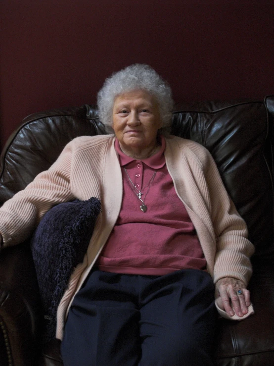 a woman with a pink sweater sitting on a brown leather chair