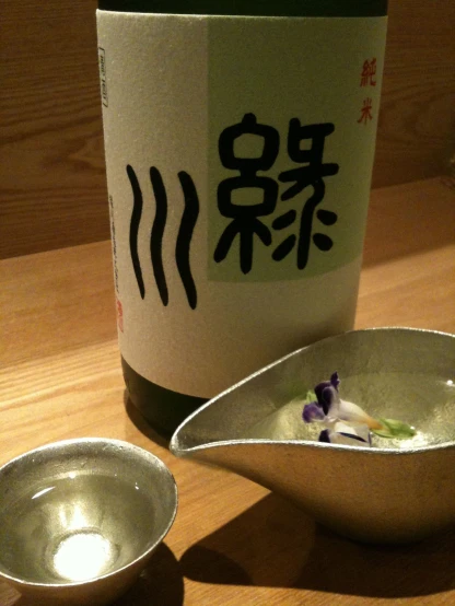 a bottle of sake and two bowls with sushi sauce on a wooden table