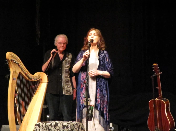 woman sings while man plays the harp behind her