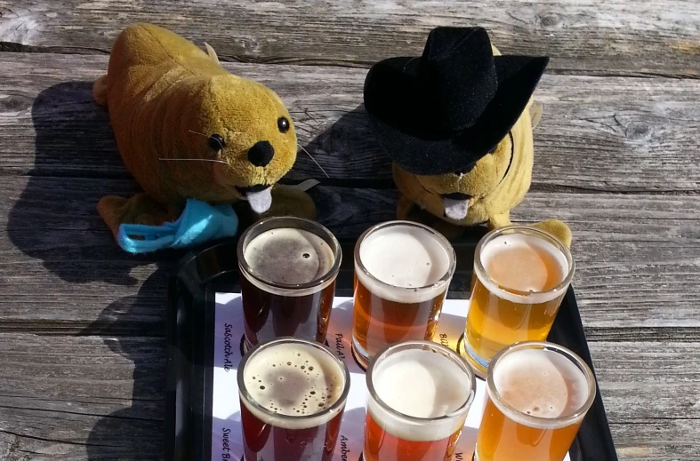 a small teddy bear with beer in a cup beside it