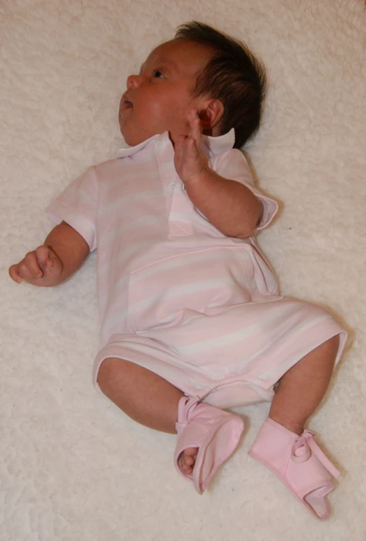 a baby with pink boots and one hand on her chest, laying on the floor