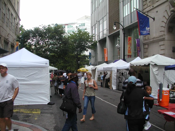 some people are walking on the street near many tents