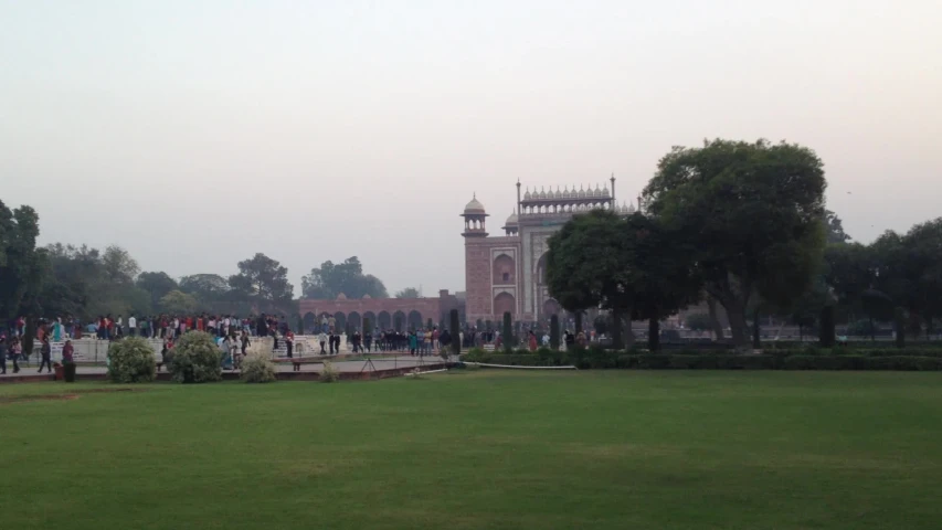 people are standing around in the grass near a clock tower