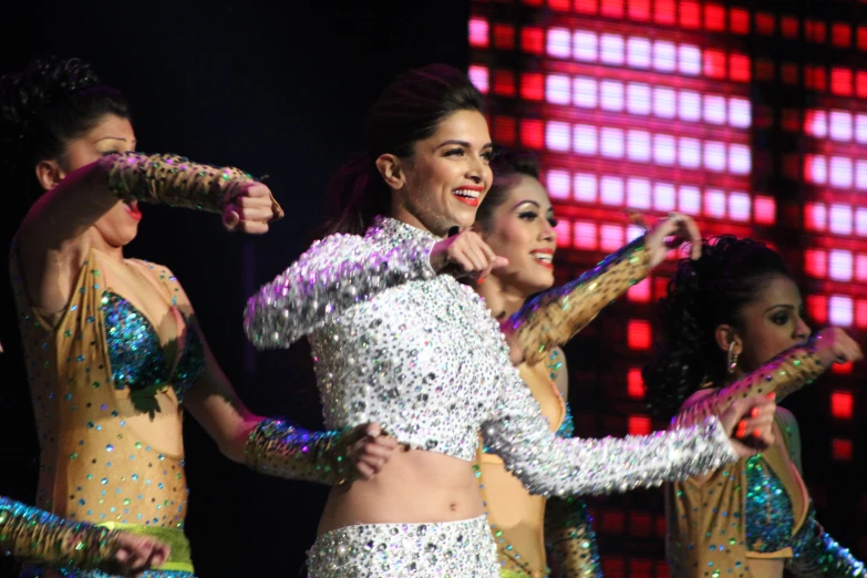 a woman dancing on stage wearing a variety of silver and green sequins