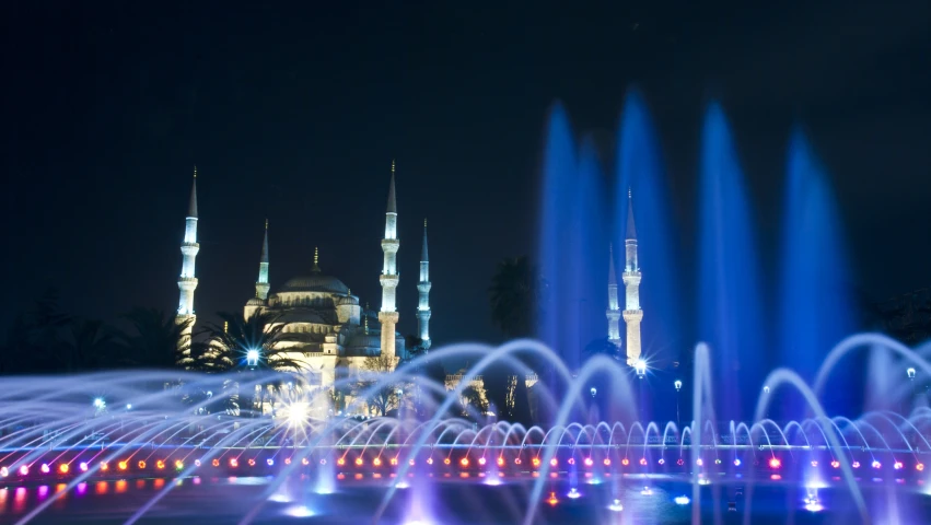 a colorful fountains show in front of a blue mosque at night