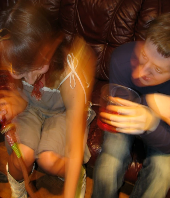 two people are sitting on a couch holding glassware