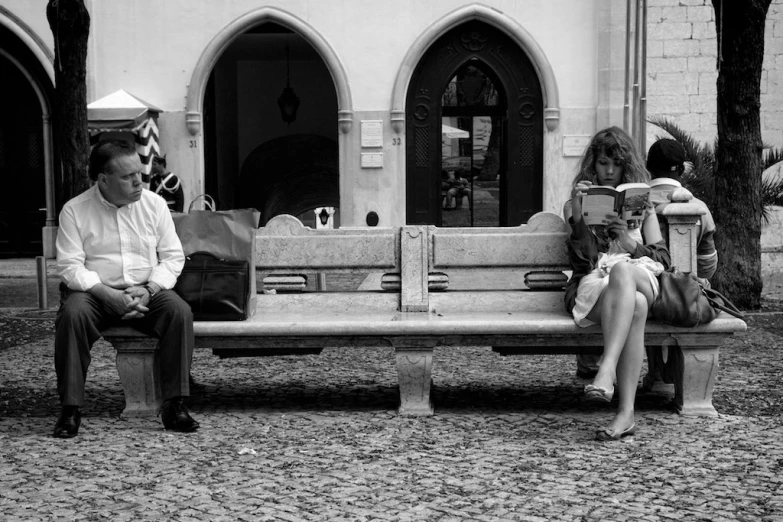 three people sitting on a bench, all looking at the same paper