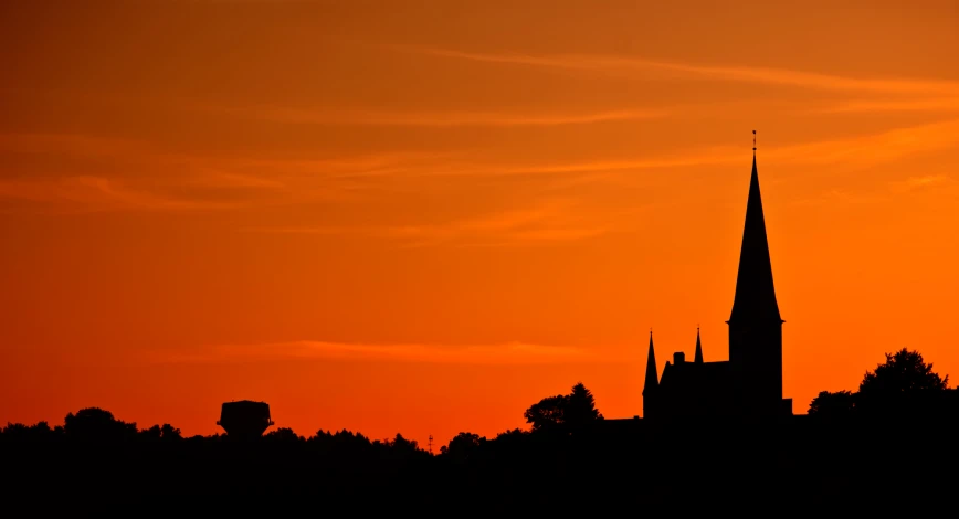 a church spire silhouetted against an orange sky at sunset