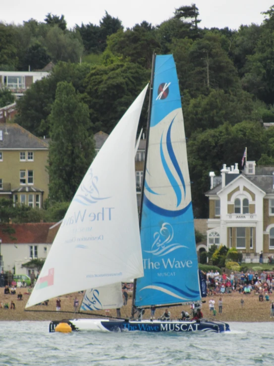 a sail boat sailing down a river in front of a town