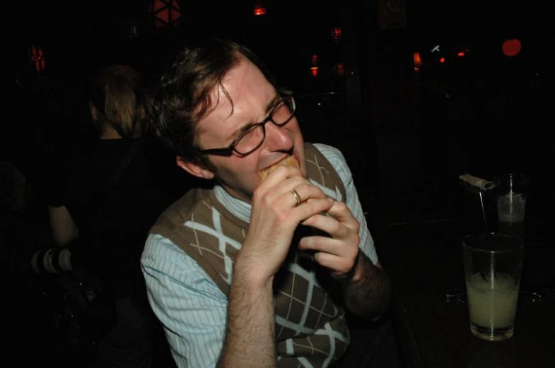 a young man in glasses eating food at a table