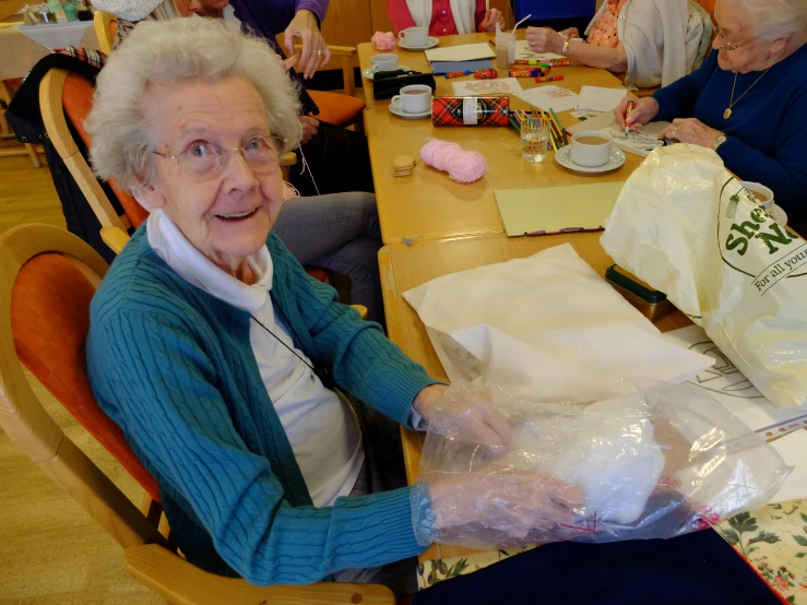 an elderly lady sitting at a table getting her tea ready to serve