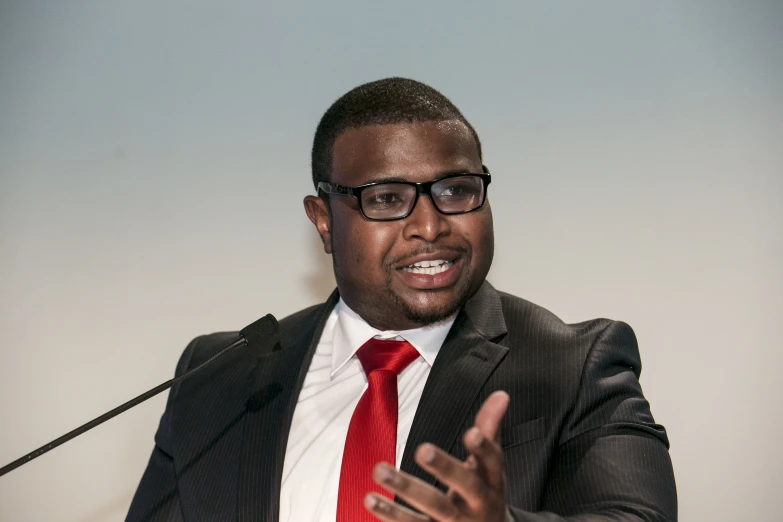 a man wearing glasses talking into a microphone