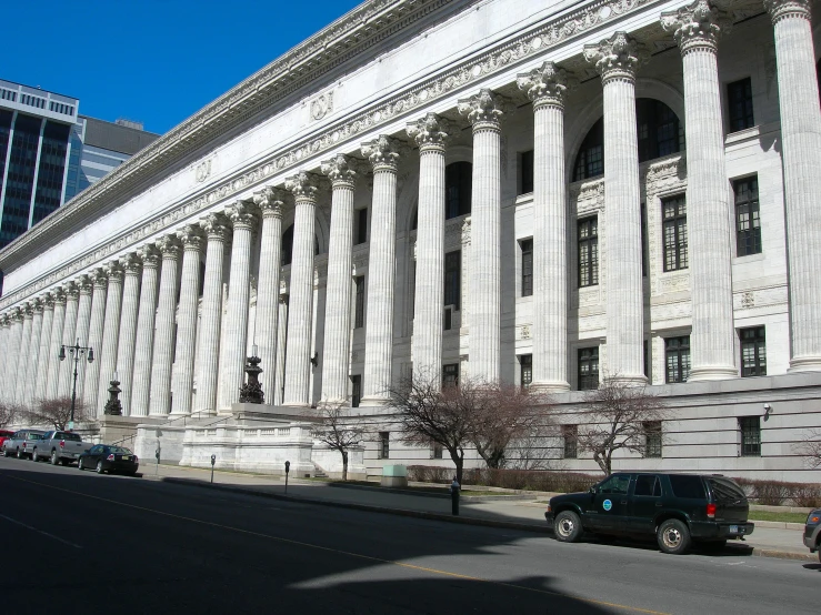 cars driving past a large building with columns