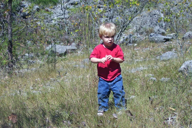 a little boy standing in a field looking down at soing