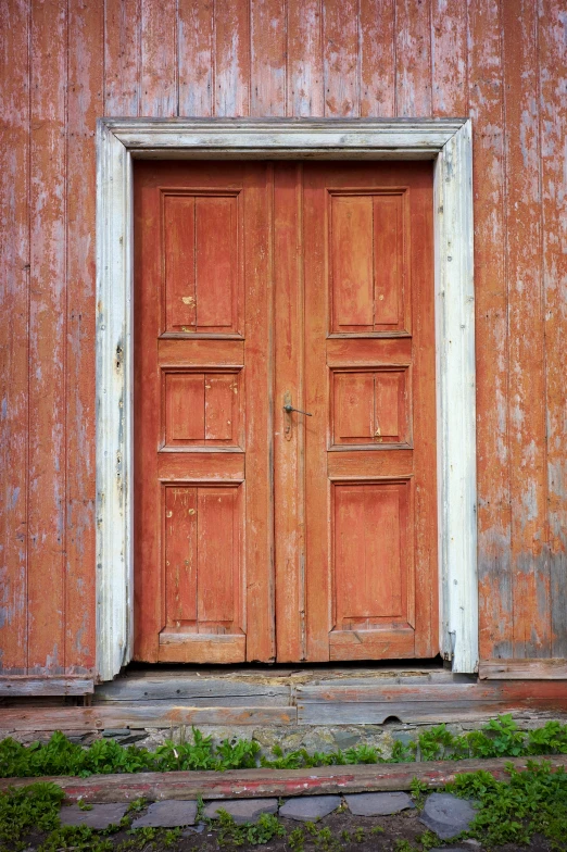 a red door is painted and surrounded by green grass