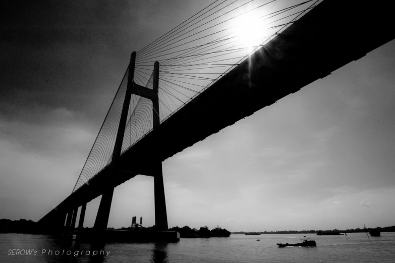 black and white image of sun shining behind the humong bridge