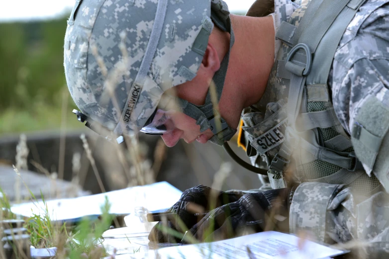 a soldier looks over his laptop in a field