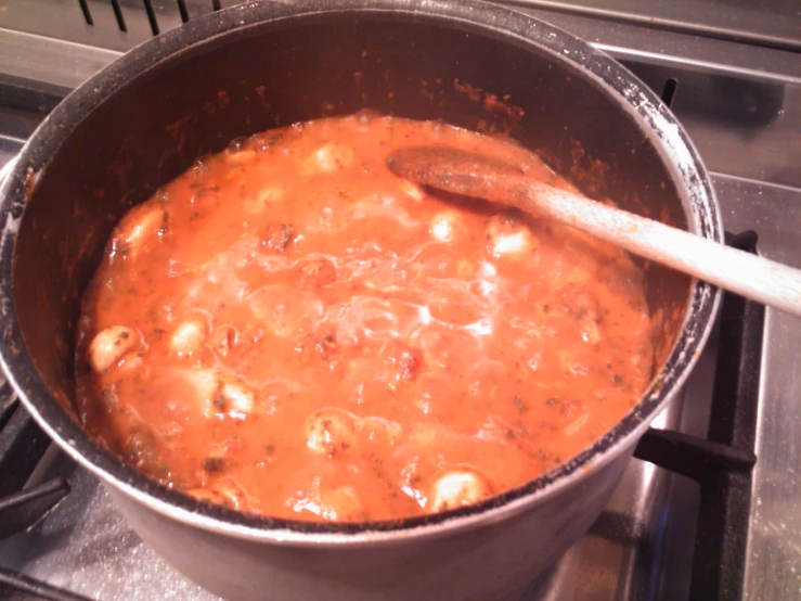 a silver pot with food and wooden spoon on top of it