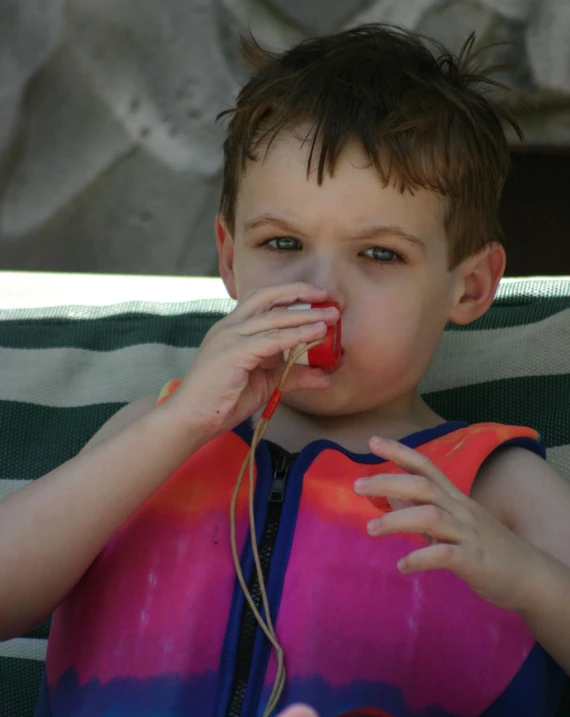 a child is blowing on his string while wearing an orange vest