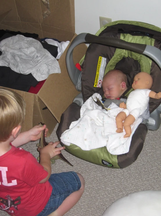 a little boy is sitting on the floor next to a baby in a stroller