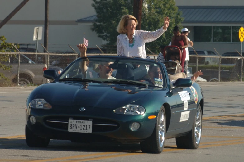 the woman waves as she drives her car with flags in front