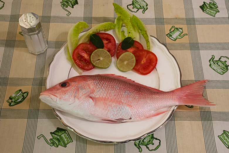 a fish, lemon wedges, tomatoes and cucumbers on a plate